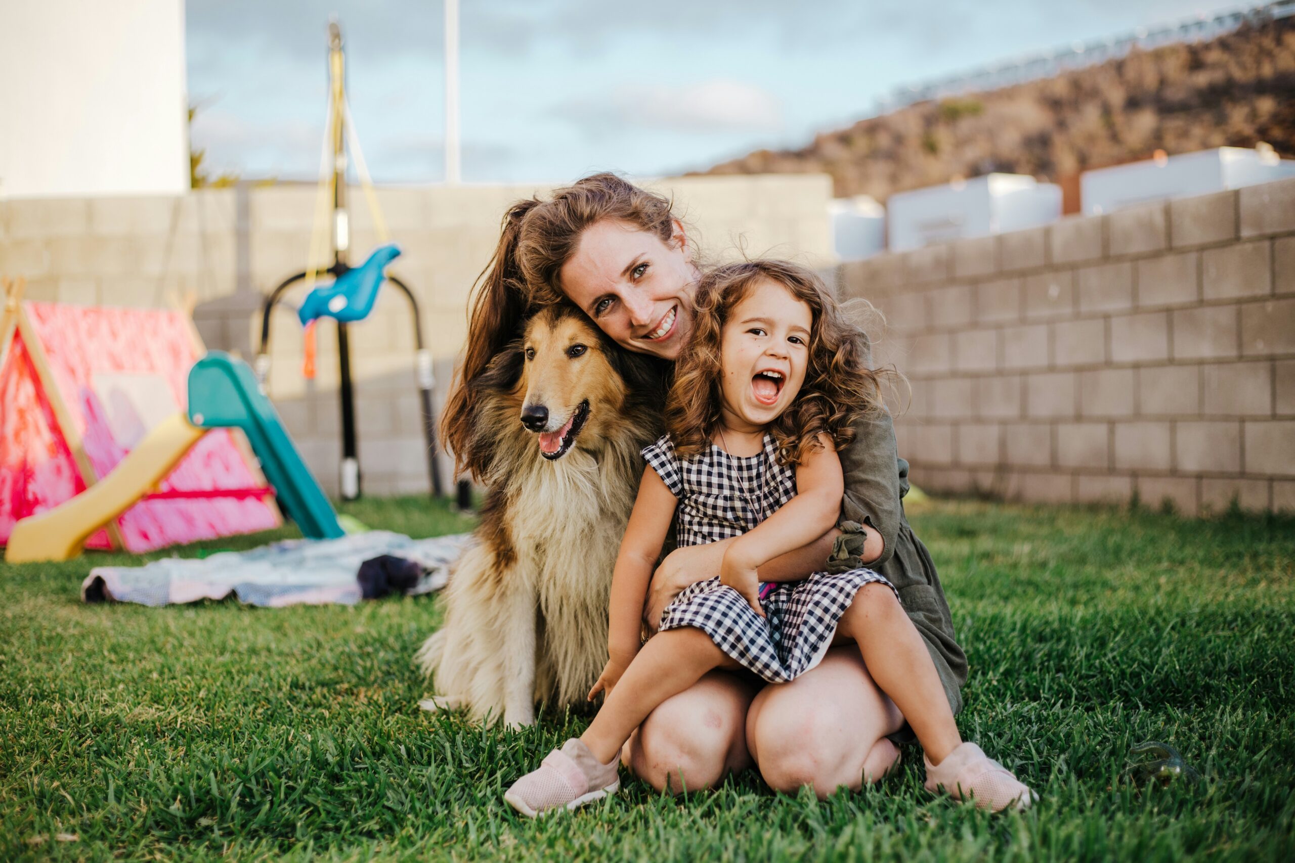 Happy mother and daughter hugging their golden retriever in the backyard of a pet-friendly rental.